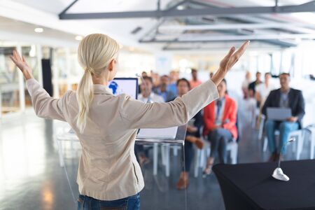 Rear view of caucasian female speaker speaks in a business seminar. International diverse corporate business partnership conceptの写真素材