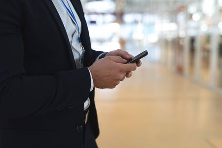 Mid section close-up of young Caucasian businessman using mobile phone in a modern office....