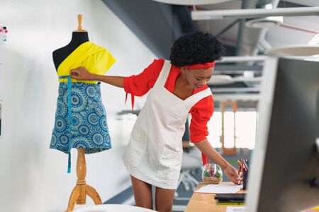 Front view of beautiful young mixed-race female fashion designer using measuring table on a mannequin in design studio. Modern casual creative fashion design business conceptの写真素材