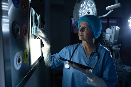 Front view of Caucasian female surgeon examining x-ray on light box in operating room at hospital....