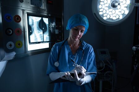 Front view of Caucasian female surgeon writing on clipboard in operating room at hospital. Shot in...