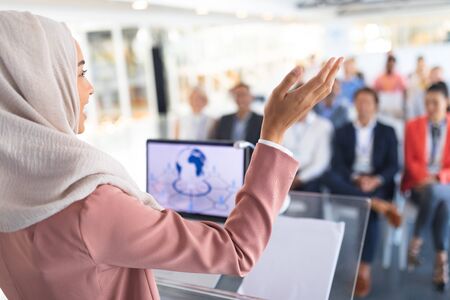 Close-up of beautiful mixed-race female speaker in hijab giving speech in a business seminar....