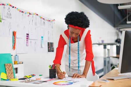 Front view of beautiful mixed-race female fashion designer drawing a sketch at desk in design studio. Modern casual creative fashion design business conceptの写真素材