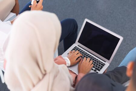 High angle view of mixed-race businesswoman in hijab working on laptop in business seminar. International diverse corporate business partnership conceptの写真素材