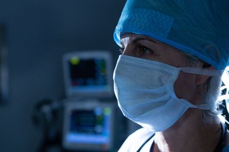 Close-up of Caucasian female surgeon with surgical mask looking away in operating room at hospital....