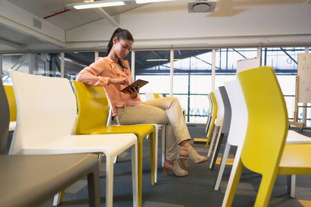 Side view of young pretty mixed-race businesswoman using digital tablet in the conference room at...