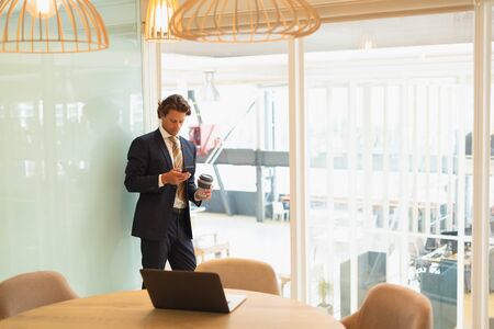 Front view of handsome young Caucasian businessman using mobile phone while having coffee in the conference room at office. New start-up business with entrepreneur working hardの写真素材