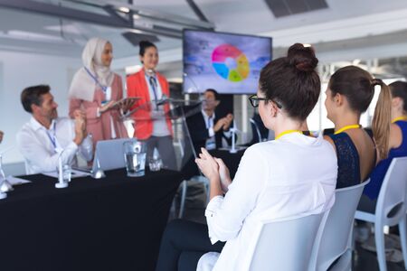 Rear view of caucasian Audience applauding while female speaker speaks in a business seminar. International diverse corporate business partnership conceptの写真素材