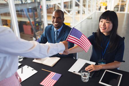 Front view of diverse  Business people holding an American flag at conference registration table. International diverse corporate business partnership conceptの写真素材
