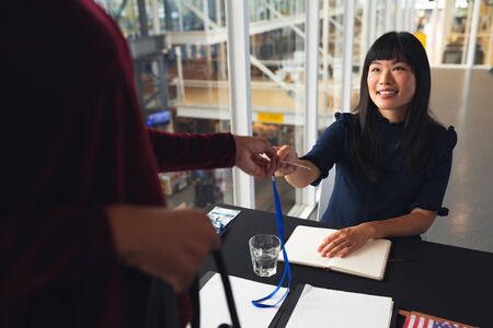 Front view of Asian female executive giving employee id to Businesswoman at conference registration table. International diverse corporate business partnership conceptの写真素材
