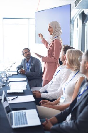 Side view of mixed race businesswoman in hijab giving presentation at table in business seminar. International diverse corporate business partnership conceptの写真素材