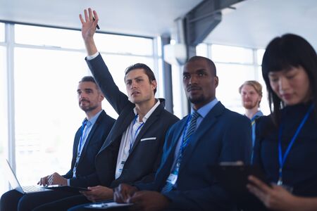 Side view of diverse Businessman raising his hand while attending business seminar in conference meeting. International diverse corporate business partnership conceptの写真素材