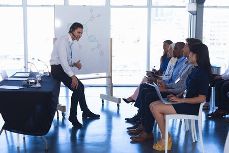 Side view of Caucasian Businessman giving presentation on flip chart in business seminar at...