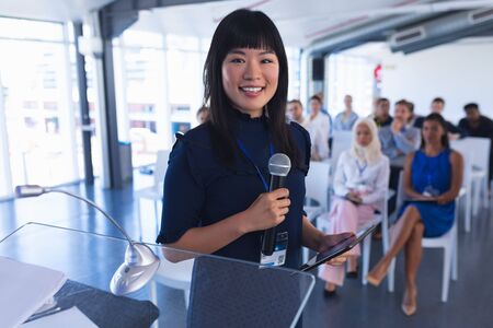 Portrait of asian female speaker with digital tablet speaks in business seminar. International diverse corporate business partnership conceptの写真素材