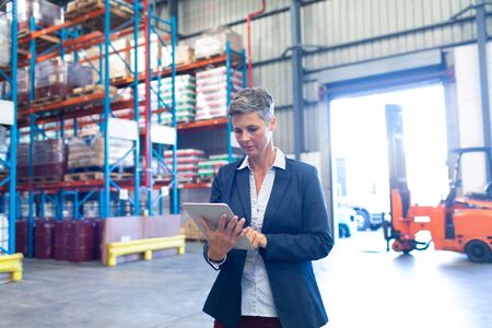 Front view of pretty mature Caucasian female manager using digital tablet in warehouse. This is a freight transportation and distribution warehouse. Industrial and industrial workers conceptの写真素材