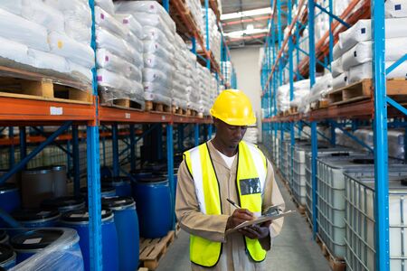 Front view of African-american male worker writing on clipboard in warehouse. This is a freight transportation and distribution warehouse. Industrial and industrial workers conceptの写真素材