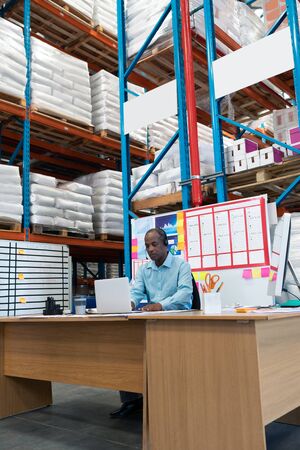 Front view of handsome mature African-american male supervisor working on laptop at desk in...
