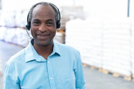 Close-up of handsome mature African-american male supervisor with headset standing in warehouse....