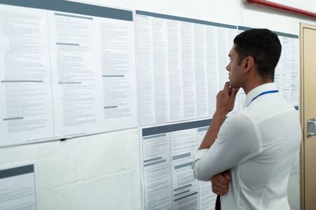 Side view of handsome young mixed-race male supervisor looking at inventory records on wall. This is...