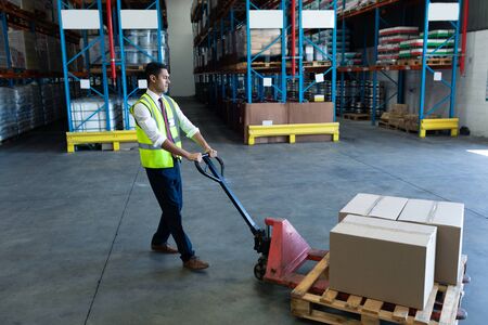 Side view of Caucasian male staff using pallet jack in warehouse. This is a freight transportation and distribution warehouse. Industrial and industrial workers conceptの写真素材