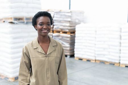 Portrait of happy pretty African-american female worker looking at camera in warehouse. This is a freight transportation and distribution warehouse. Industrial and industrial workers conceptの写真素材