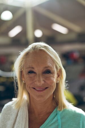 Portrait close-up of happy active senior Caucasian woman looking at camera in fitness studio. Strong...