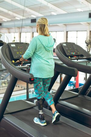 Rear view of disabled active senior Caucasian woman with leg amputee exercising on treadmill in...