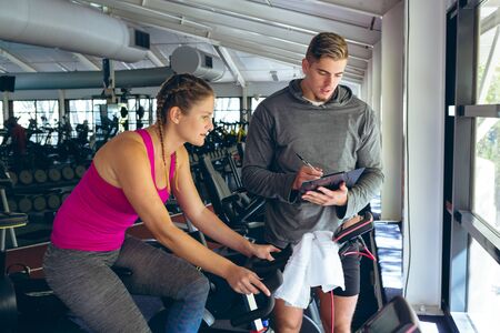 Front view of young Caucasian Male trainer assisting Caucasian female athlete with exercise in...