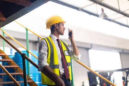 Side view of Caucasian Male supervisor talking on talkie walkie on stairs in warehouse. This is a...