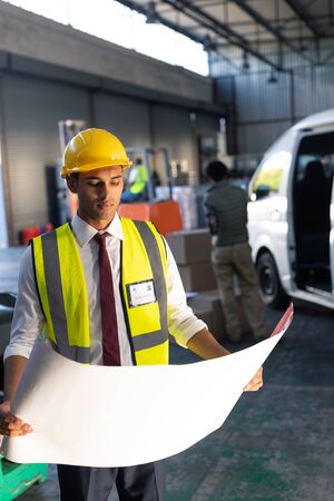 Front view of Caucasian male supervisor looking at blueprint in warehouse. This is a freight...