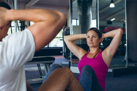 Side view of young fit Caucasian male and female athletic exercising together in fitness center....
