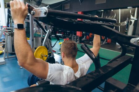 Rear view of handsome young Caucasian man exercising with ab crunch machine in fitness studio....