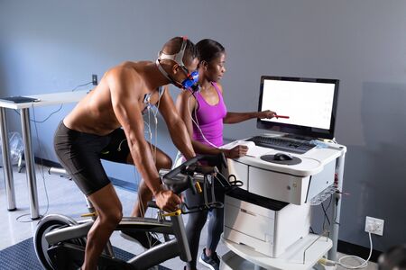 Side view of a naked African-American athletic man doing a fitness test using a mask connected to a...