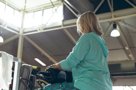 Low angle view of disabled active senior Caucasian woman exercising with leg curl machine in fitness...