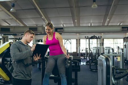 Front view of handsome young Caucasian male trainer discussing with pretty young Caucasian female...