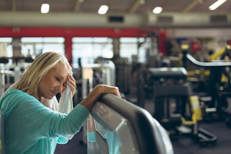 Side view of tired active senior Caucasian woman wiping sweat towel in fitness studio. Strong active...