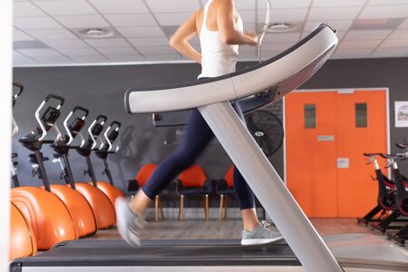 Side view of a Caucasian athletic woman exercising using treadmill inside a room at a sports center....