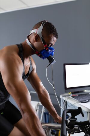 Side view of an African-American athletic man doing a fitness test using a mask connected to a...