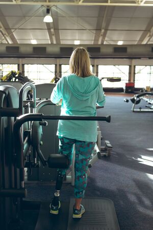 Rear view of disabled active senior Caucasian woman with amputee leg exercising in fitness studio....