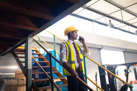 Side view of Caucasian Male supervisor talking on talkie walkie on stairs in warehouse. This is a...