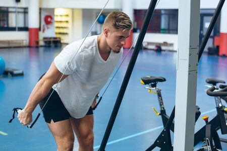 Side view of young fit Caucasian male athlete doing triceps exercise in fitness studio. Bright...