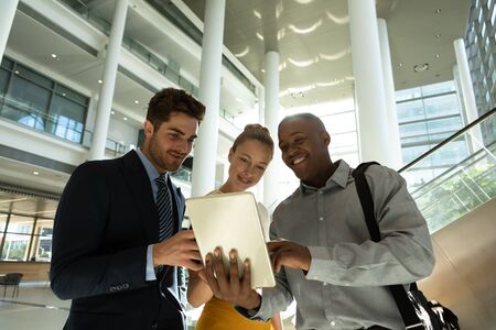 Low angle front view of a young African American businessman holding tablet computer and showing it...