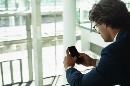 Close-up of businessman leaning on railing and using mobile phone in a modern office building. Modern corporate start up new business concept with entrepreneur working hardの写真素材