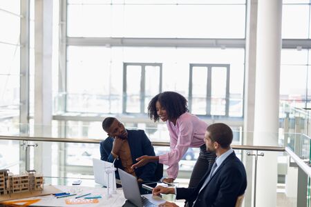 Elevated side view of young African American businesswoman standing at a desk talking with a young...