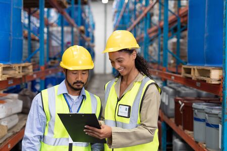 Front view of male and female worker discussing on clipboard in warehouse. This is a freight transportation and distribution warehouse. Industrial and industrial workers conceptの写真素材