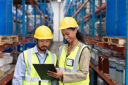 Front view of male and female worker discussing on clipboard in warehouse. This is a freight transportation and distribution warehouse. Industrial and industrial workers concept