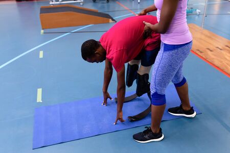 Side view of African-american female trainer assisting disabled African-american man while...