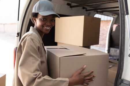 Happy delivery woman unloading cardboard boxes from a van outside the warehouse. This is a freight transportation and distribution warehouse. Industrial and industrial workers conceptの写真素材