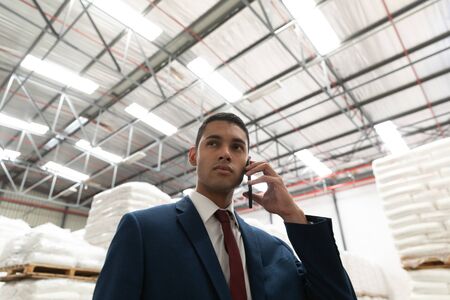 Low angle view of businessman talking on mobile phone in warehouse. This is a freight transportation...