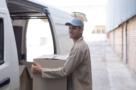 Side view of delivery man carrying cardboard boxes outside the warehouse. This is a freight...